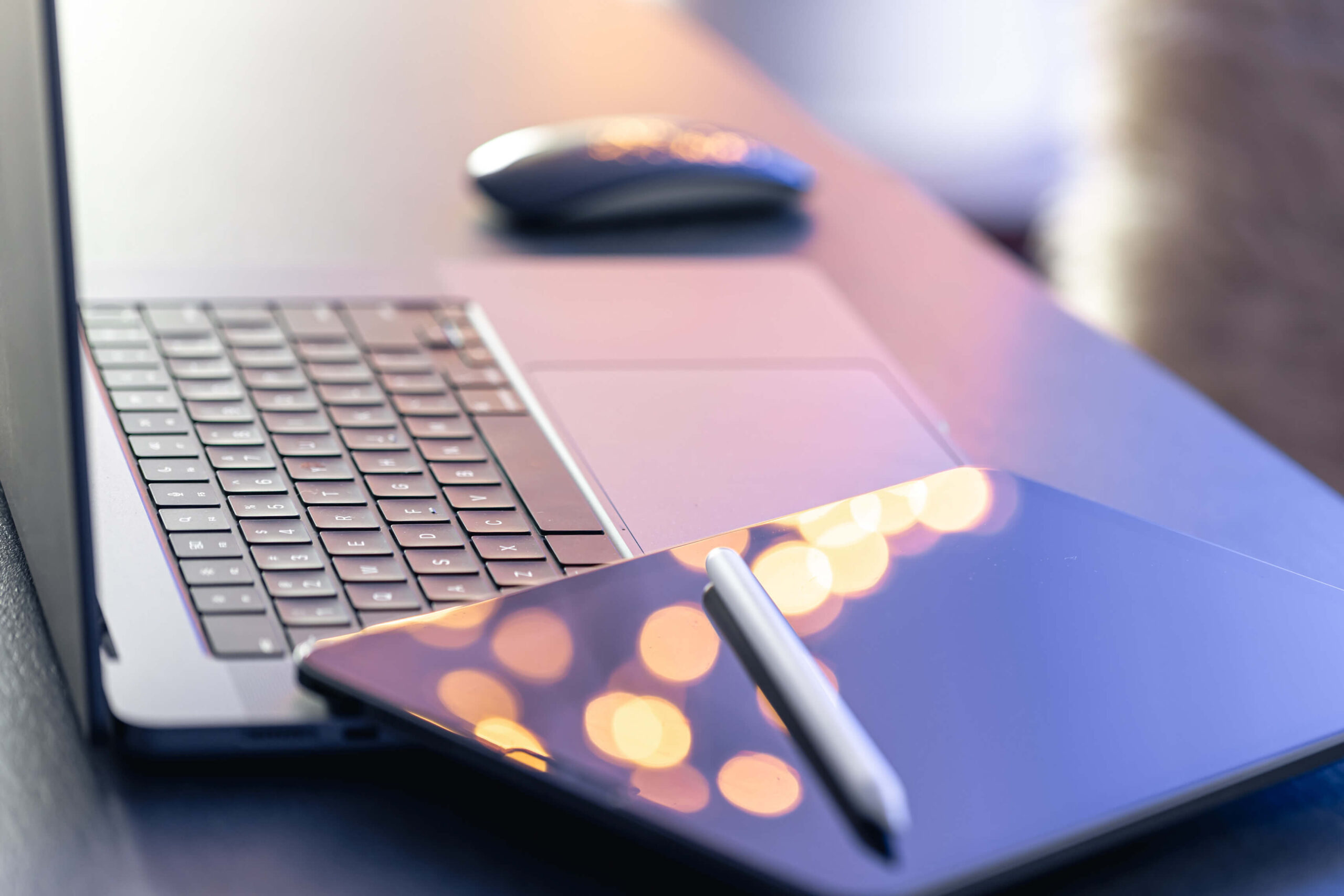 Bezprzewodowa myszka, otwarty laptop i tablet z wysikiem, w którym odbijają się drobne światełka. Ilustracja do wpisu pod tytułem Czytelność wpisu blogowego