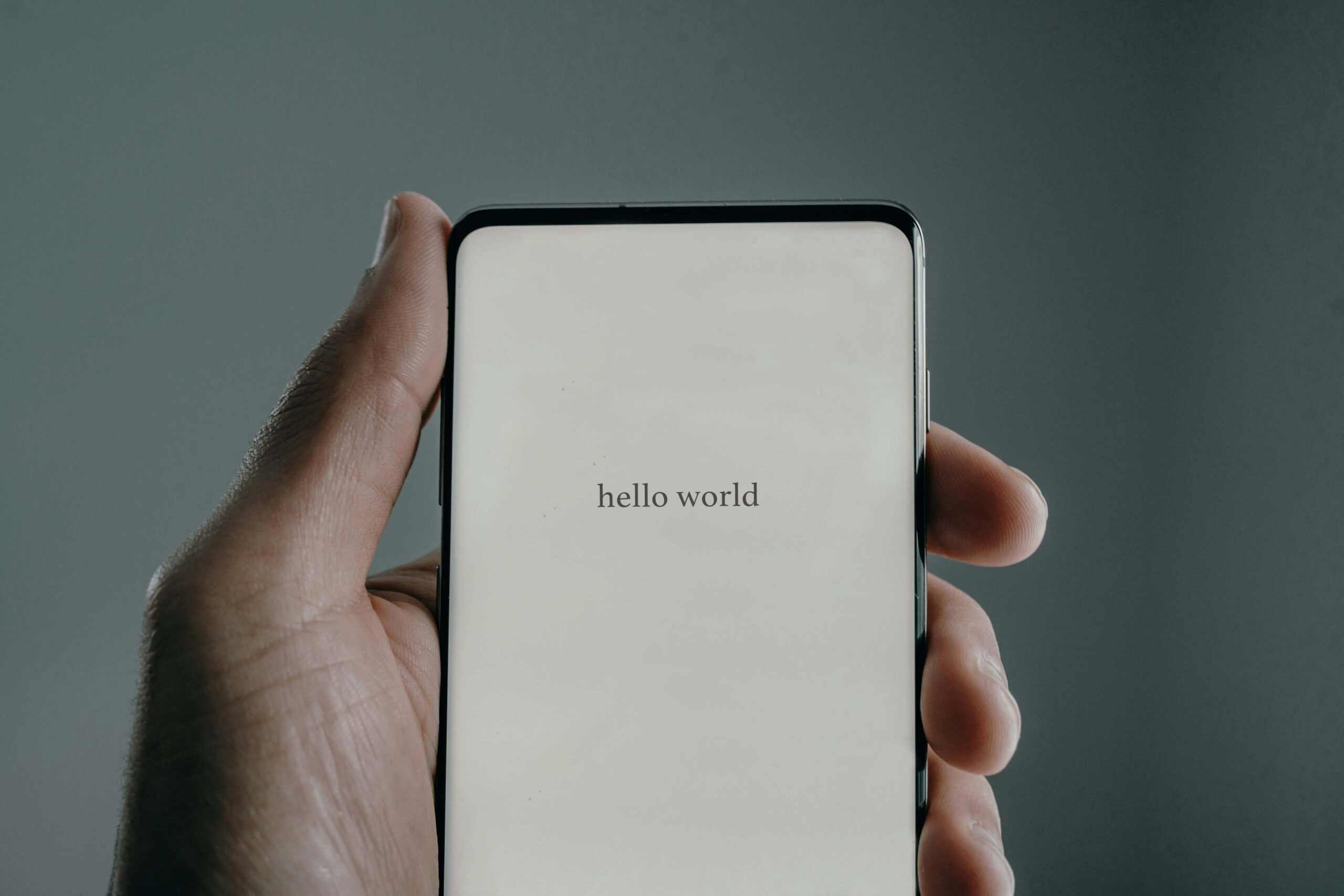 Lewa dłoń trzymająca smartfon z napisem hello world na wyświetlaczu. Ilustracja do tekstu Zasada kciuka w projektowaniu