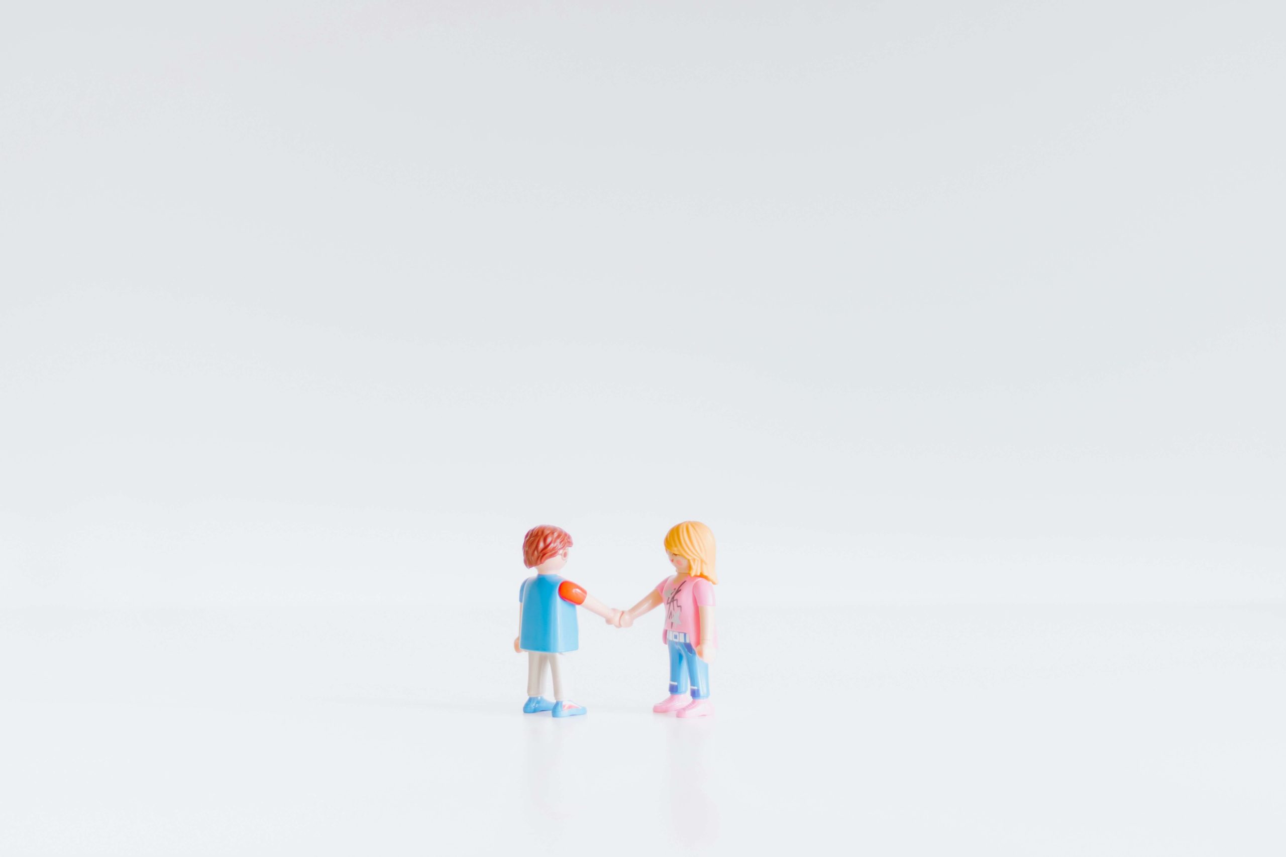 Dwie plastikowe figurki ludziki witają się uściskiem ręki. Ilustracja do tekstu Najniższa cena ever