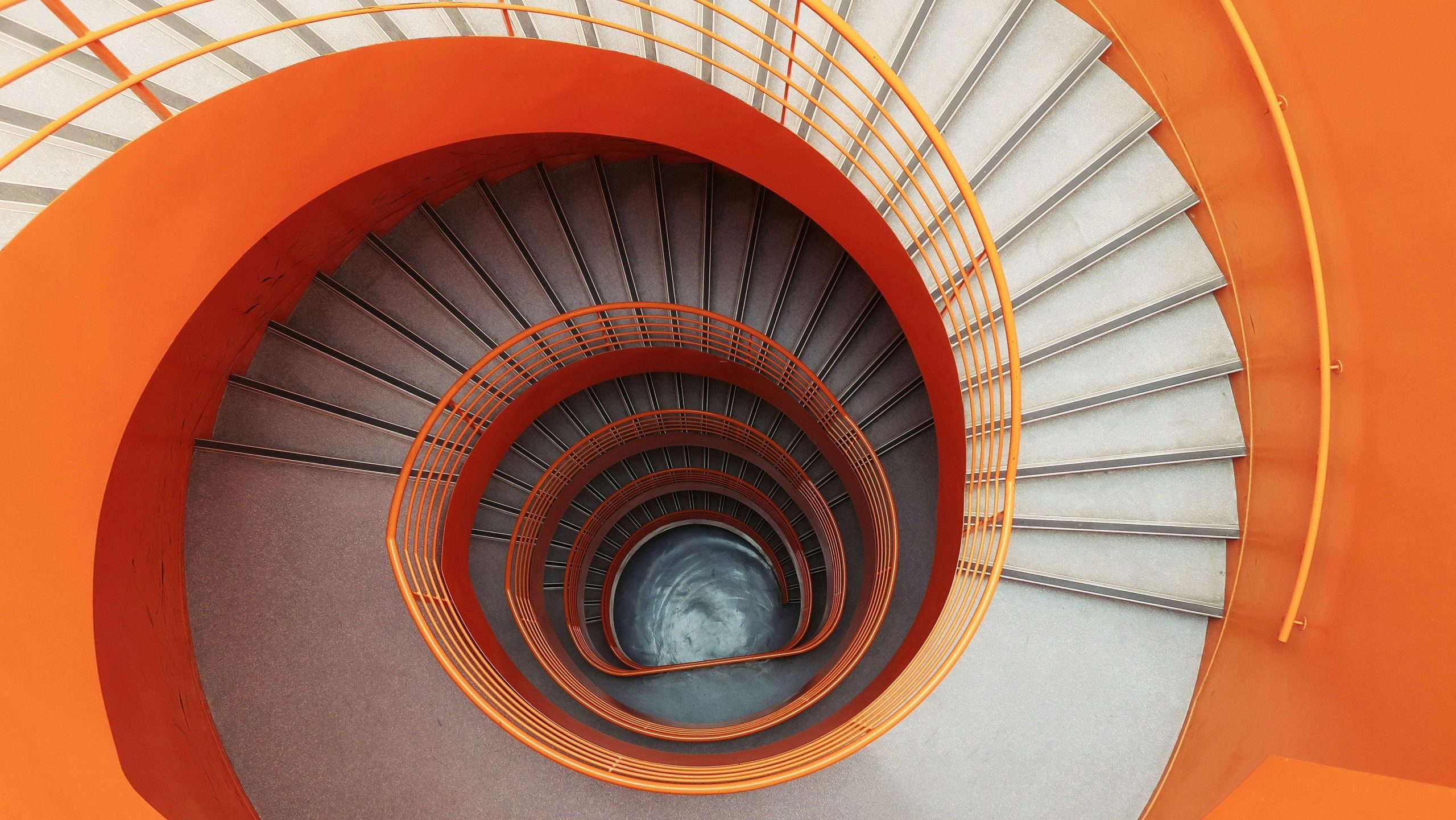 Widziane od góry zakręcające naokoło schody biało-pomarańczowe. Ilustracja do tekstu Jak się rozwijać na freelansie